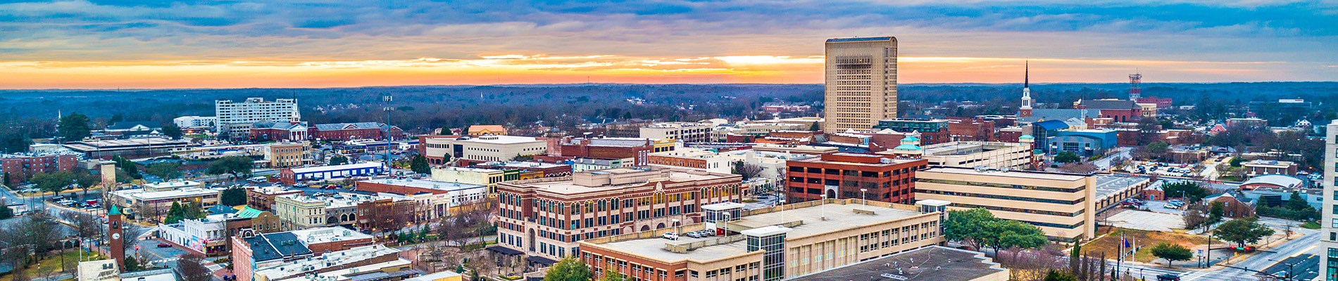 The image shows a scenic view of a city skyline at sunset with the horizon line visible between two buildings, featuring a gradient of colors from warm hues near the horizon to cooler tones higher up in the sky.