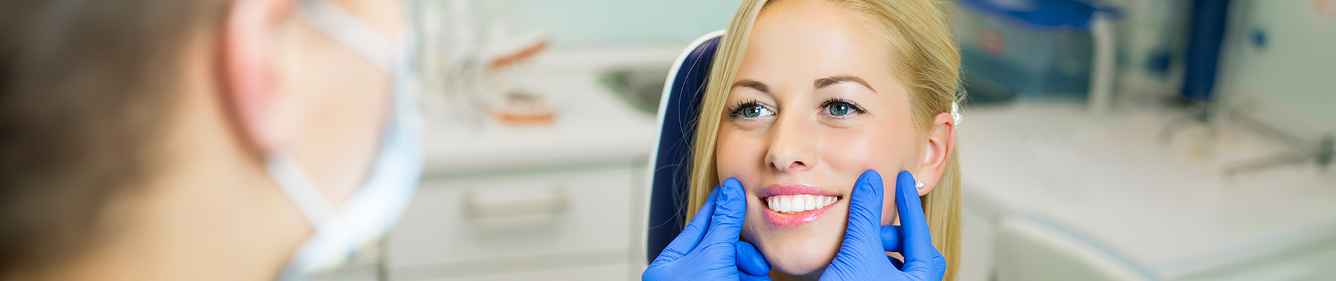 A person is seated in a dental chair, receiving care from a dental professional who stands behind them.