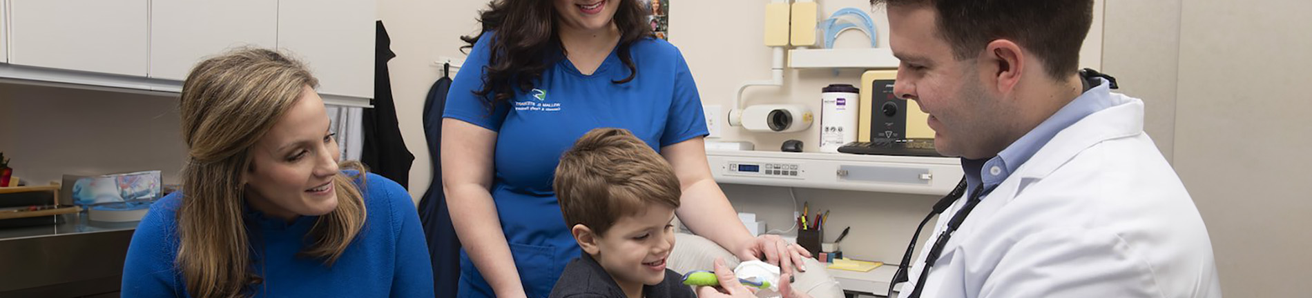 The image depicts a group of people in a medical setting, with a child receiving attention from a healthcare professional.