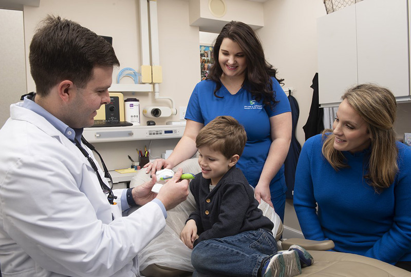 A dentist examines a child s teeth while family members look on, with a woman holding the child.