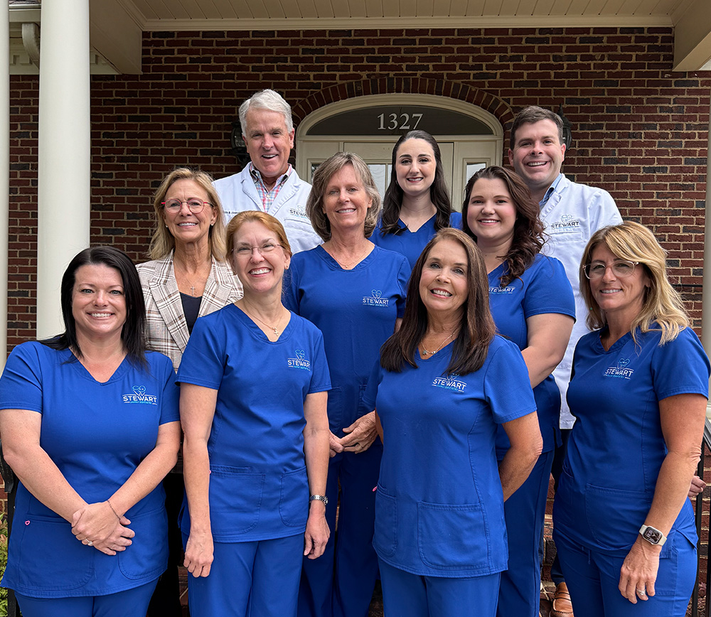 A group of healthcare professionals posing together outside a building with a brick facade and a white door frame.