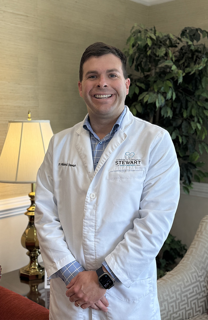 The image shows a man wearing a white lab coat standing in an office environment.